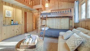 En mysig stuga med en våningssäng, en soffa, en stege och ett litet köksutrymme.