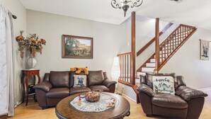 A living room with a brown leather sofa, a coffee table, a staircase, and a painting on the wall. - Close to San Antonio Zoo & Airport: Cozy Townhome (San Antonio)