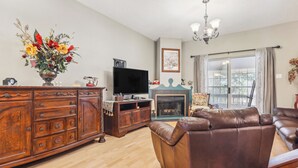 A living room with a wooden cabinet, a brown leather sofa, a flat-screen TV, and a fireplace. - Close to San Antonio Zoo & Airport: Cozy Townhome (San Antonio)
