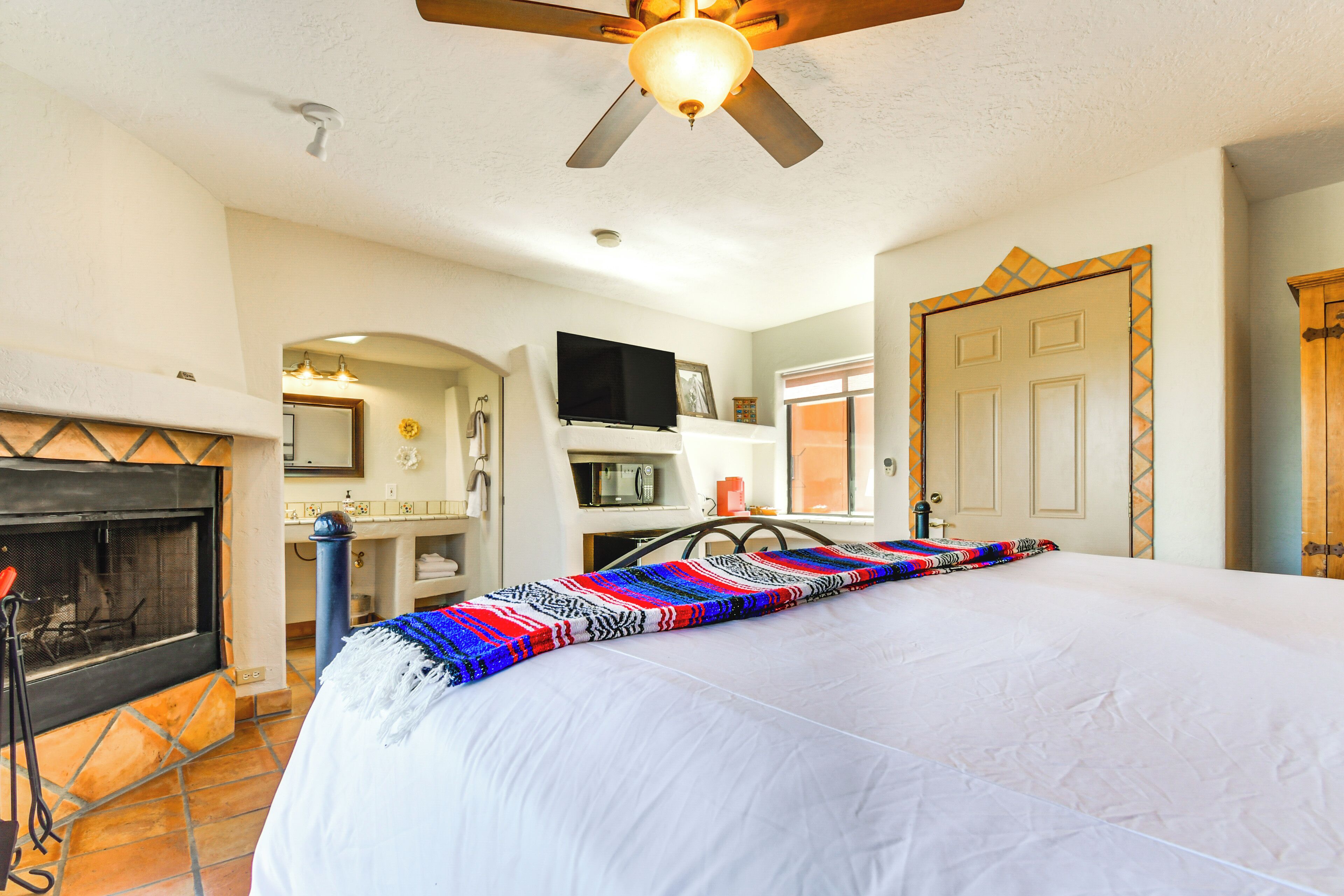 A bedroom with a large bed, a fireplace, a ceiling fan, and a door with a decorative frame.