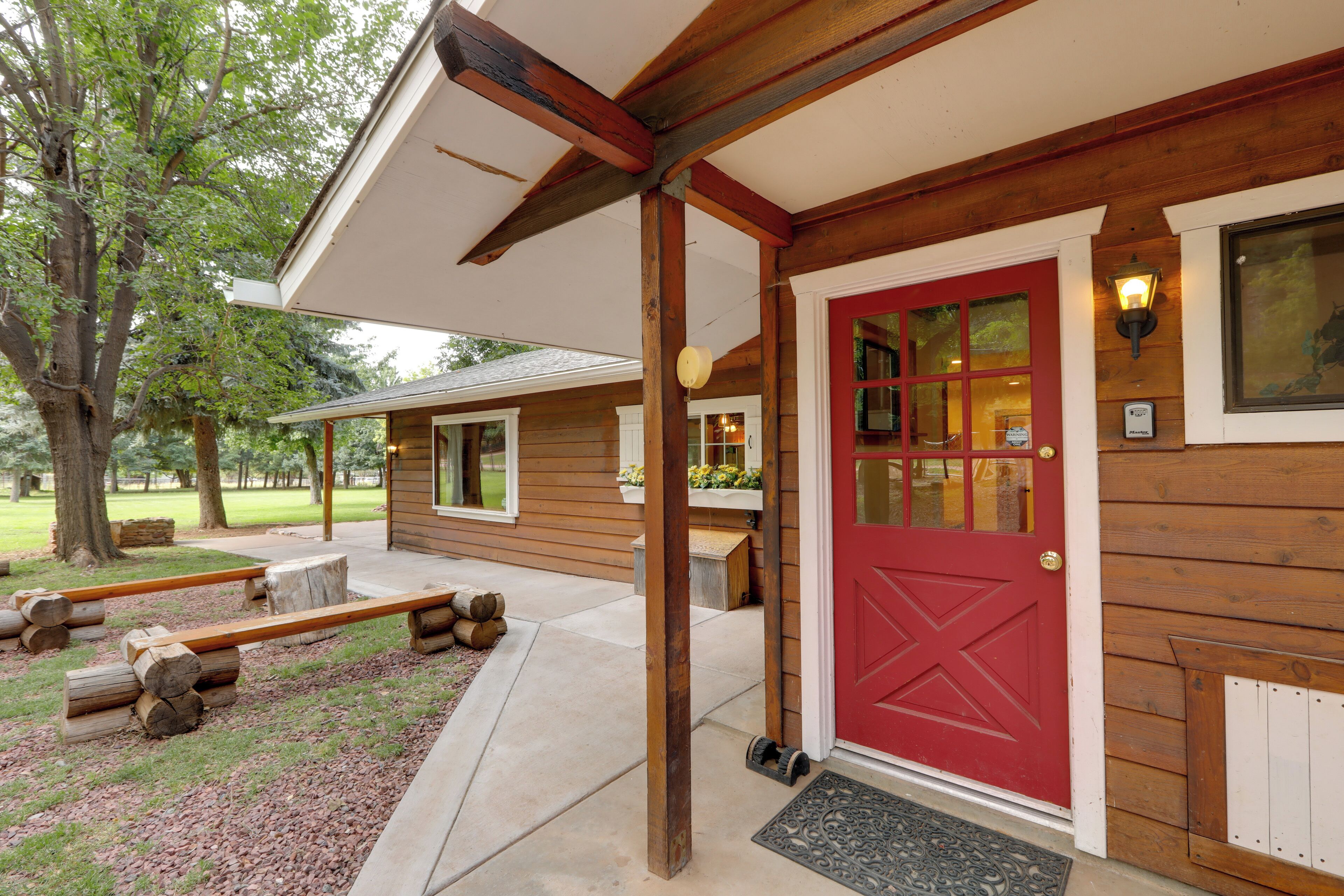 A wooden cabin with a red door, a covered porch, and a small outdoor seating area.