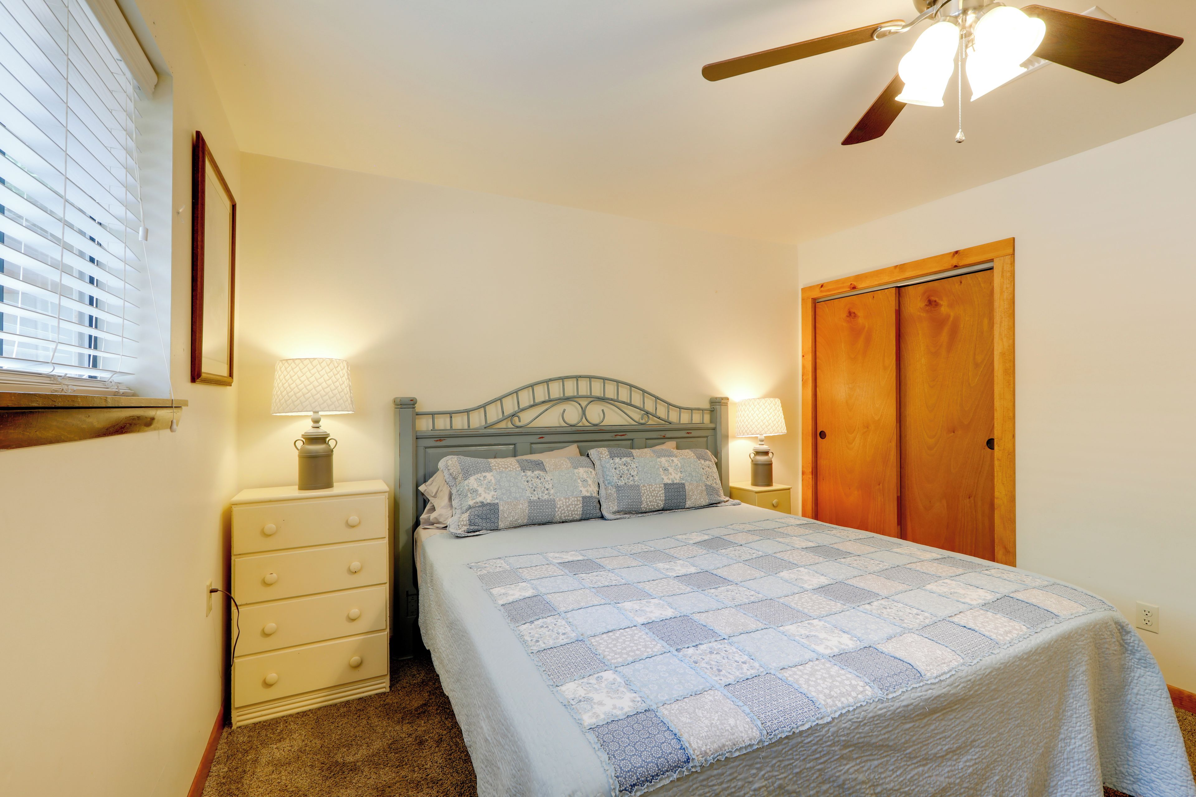 A bedroom with a bed, a nightstand, a dresser, a ceiling fan, and a wooden door.