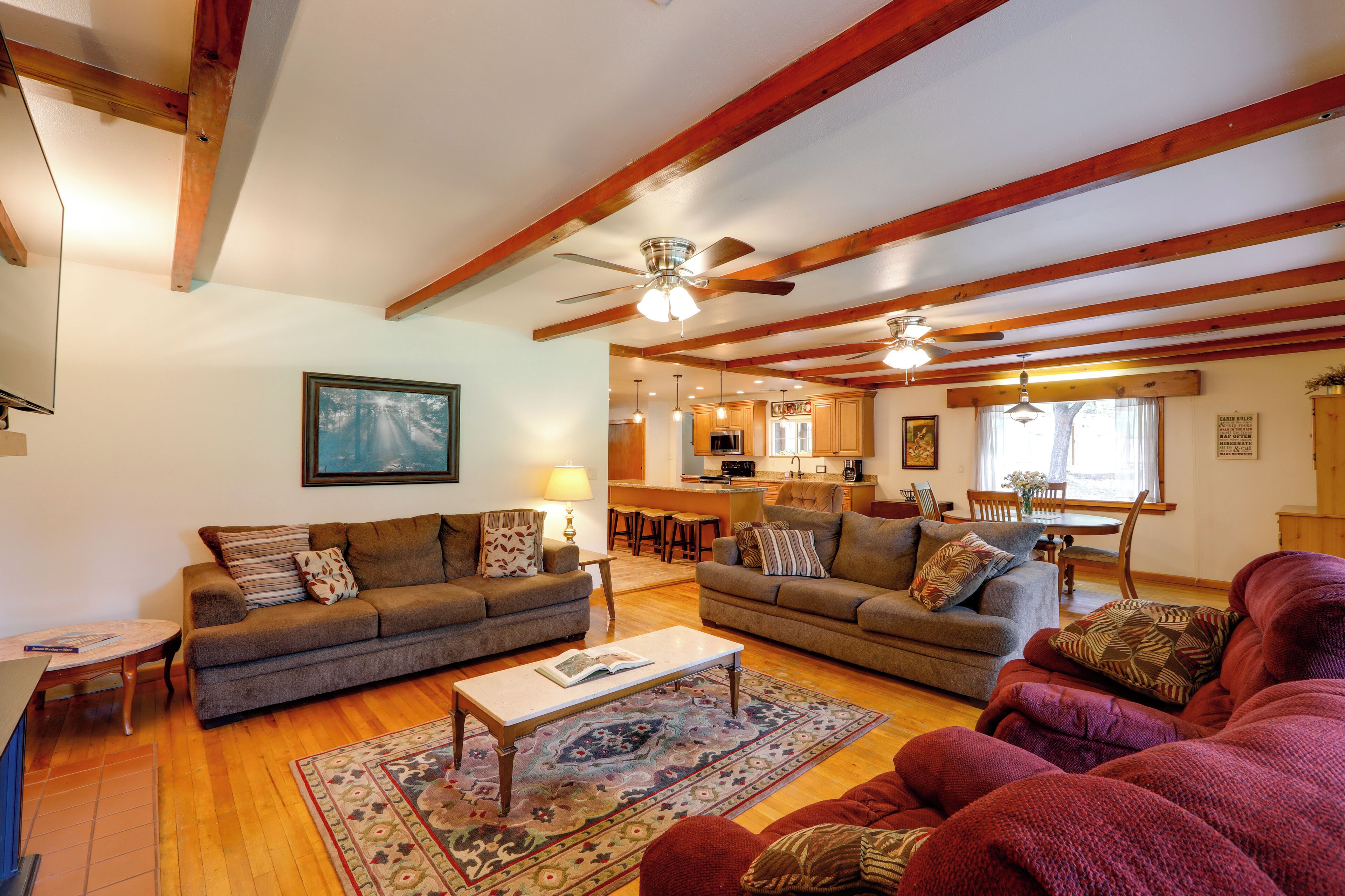 A spacious living room with two sofas, a coffee table, and a rug. There is a dining area with a table and chairs, and a kitchen in the background.