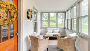 Een zonnedroom met rieten meubels, een houten deur en uitzicht op een groen landschap.