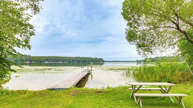 Een picknicktafel en een houten steiger die uitloopt in een rustig meer, omgeven door groen.