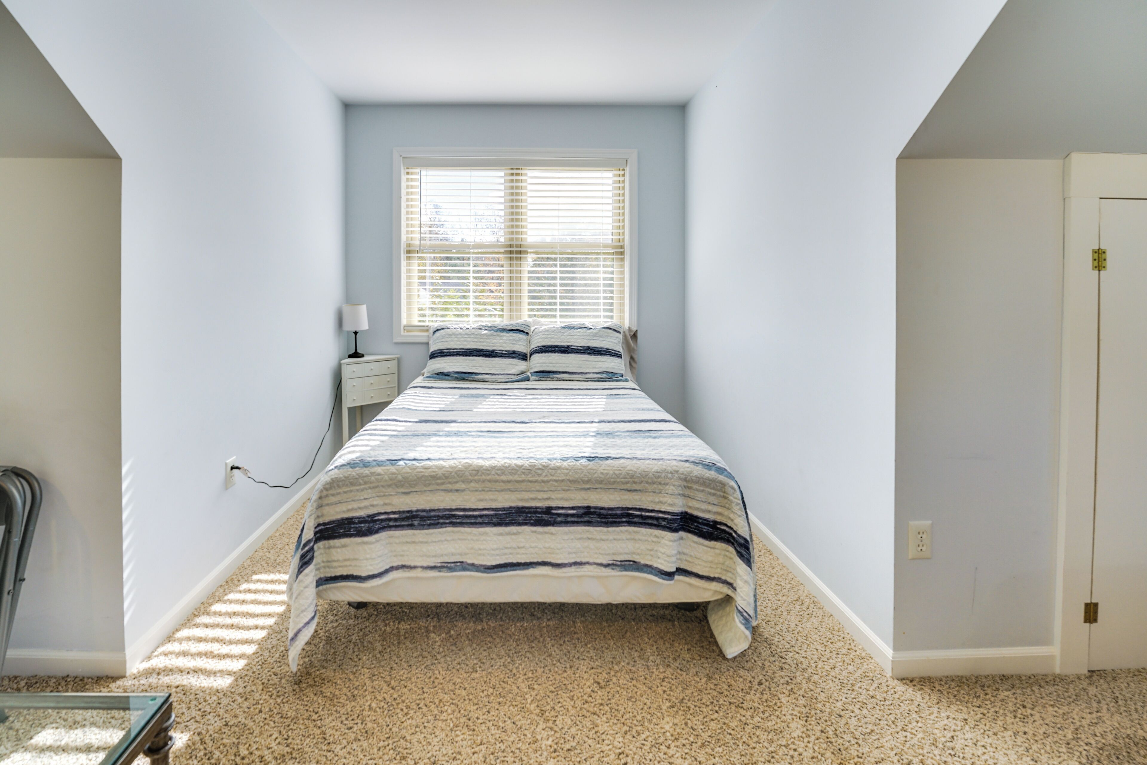 A bedroom with a bed, a nightstand, a lamp, and a window with blinds.