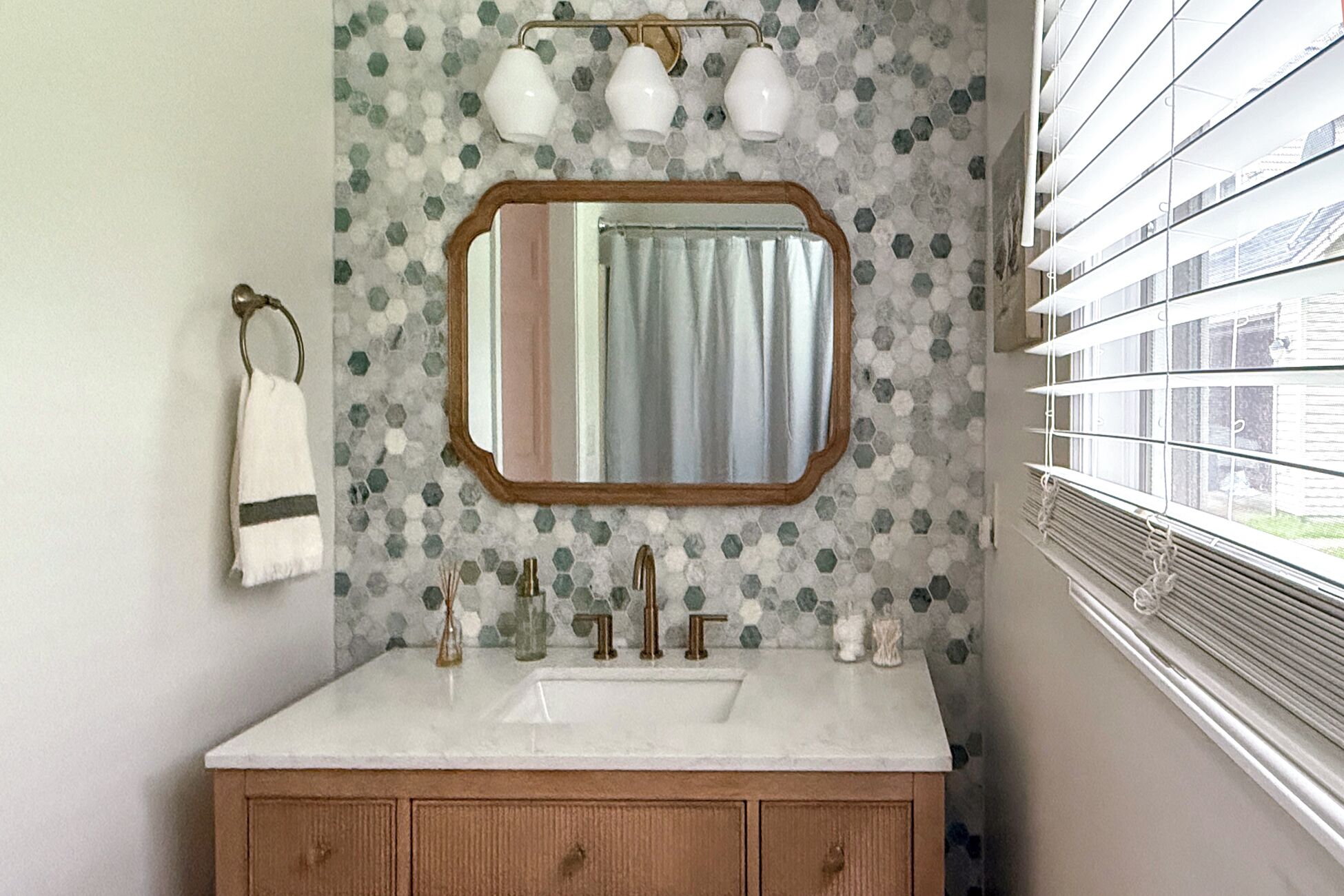 A bathroom with a white sink, a mirror with a wooden frame, a towel rack, and a window with blinds.