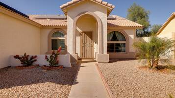 Enter through a decorative archway and into a charming home with a tiled roof, flanked by arched windows and a pathway leading to the door.