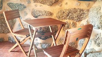 A small, rustic room with a stone wall, two wooden folding chairs, and a small table.