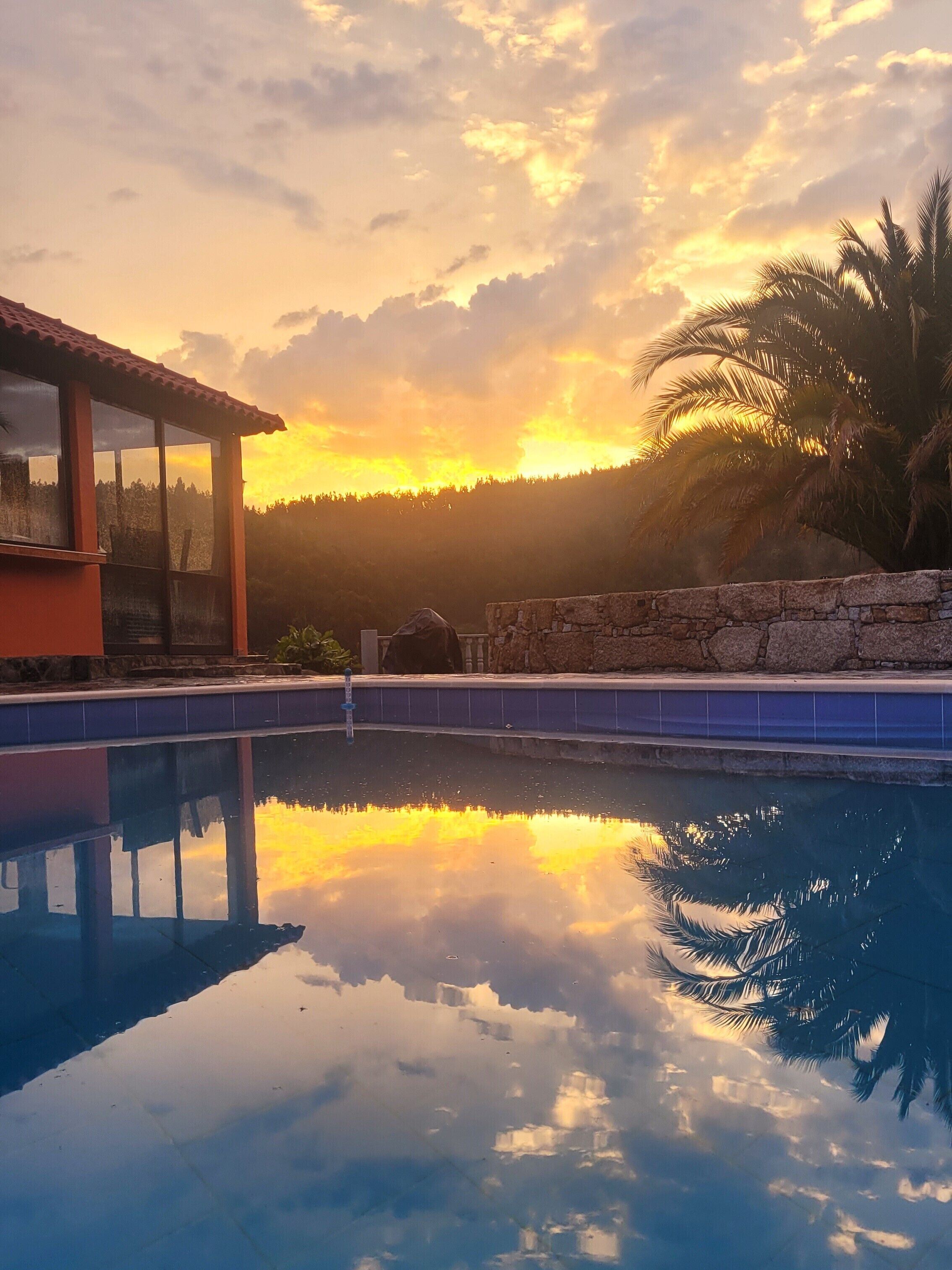 A swimming pool with a stone wall and a view of the sunset.