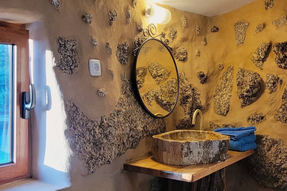 A bathroom with a stone wall, a wooden sink, and a mirror.