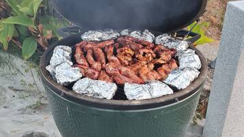 A portable grill with foil-wrapped meat, set outdoors on a stone surface.