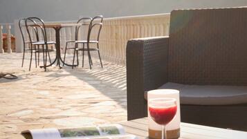 Ein Tisch mit einem Buch und einem Glas roter Flüssigkeit, Gartenmöbel aus Rattan und ein Fliesenboden.