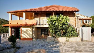 A two-story house with a stone facade, a red-tiled roof, and a balcony.