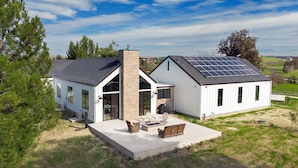 Una casa moderna con un patio amplio, paneles solares y una chimenea de piedra.