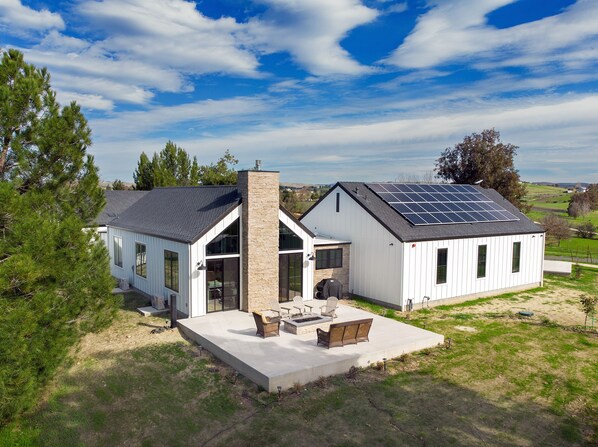 A modern house with a large patio, solar panels, and a stone chimney.