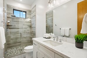 A modern bathroom with a glass-enclosed shower, a large mirror, and a marble sink.