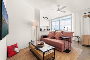 A modern living room with a sofa, a glass coffee table, a ceiling fan, and a large window offering a city view. - Best of city-suburbs living in trendy Darlinghurst (Darlinghurst)
