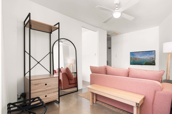 A modern room with a wooden desk, a pink sofa, a bench, and a ceiling fan.