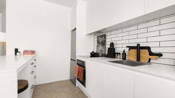 A modern kitchen with white cabinetry, a black and white tiled backsplash, and a wooden cutting board on the countertop.