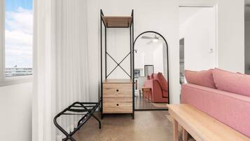 A bedroom with a bed, a bench, a desk with drawers, a mirror, and a window with curtains.