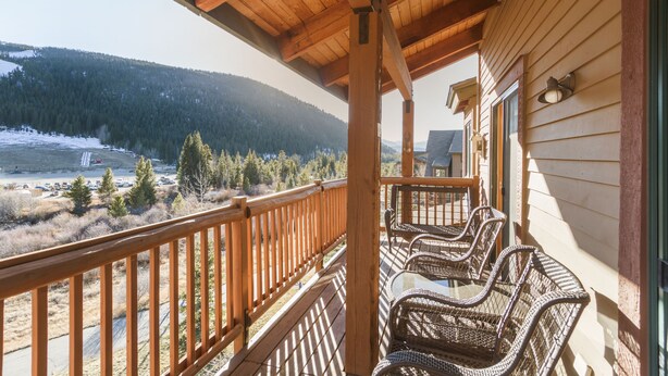 A wooden balcony with wicker chairs, overlooking a snowy landscape and a forested mountain. - Prime 3 Bedroom looking at Keystone Mtn House! (Keystone)