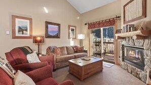 A living room with a fireplace, a sofa, a coffee table, and a view of the outdoors through a glass door. - Prime 3 Bedroom looking at Keystone Mtn House! (Keystone)