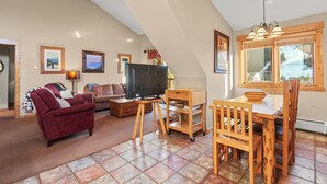 A spacious living area with a high ceiling, a wooden dining table with chairs, a sofa, a television, and artwork on the walls. - Prime 3 Bedroom looking at Keystone Mtn House! (Keystone)