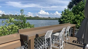 Terraza de madera con mesa y sillas blancas con vista a un cuerpo de agua.