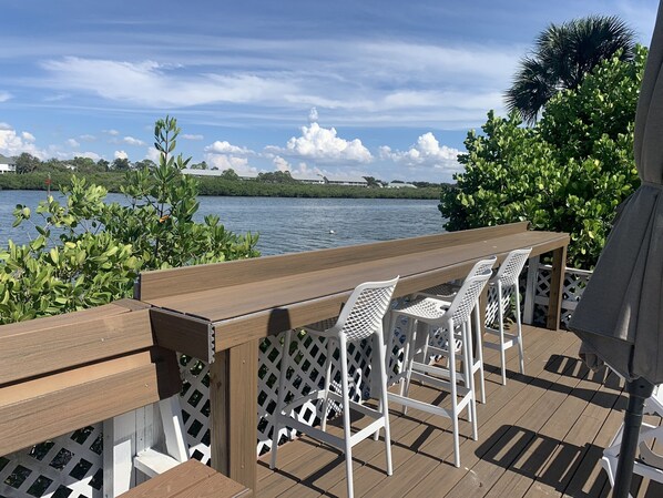 A wooden deck with a table and white chairs overlooking a body of water.