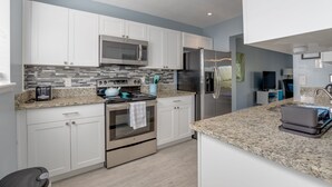 Una cocina moderna con armarios blancos, un refrigerador de acero inoxidable, un microondas y un horno empotrado.
