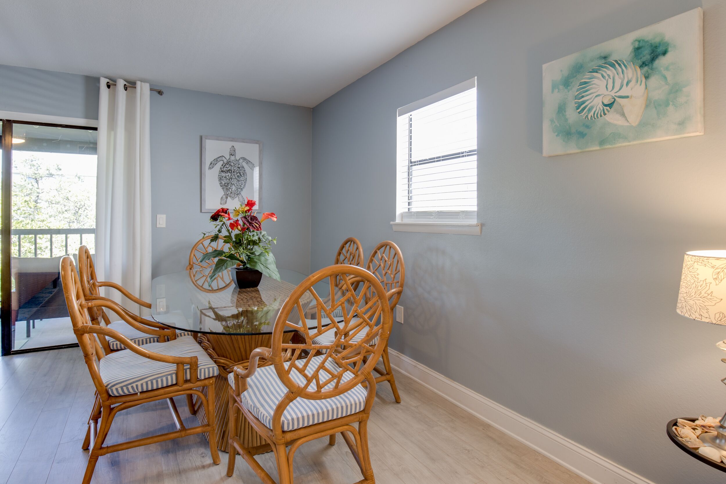 A dining area with a glass table, wicker chairs, and a vase with flowers.