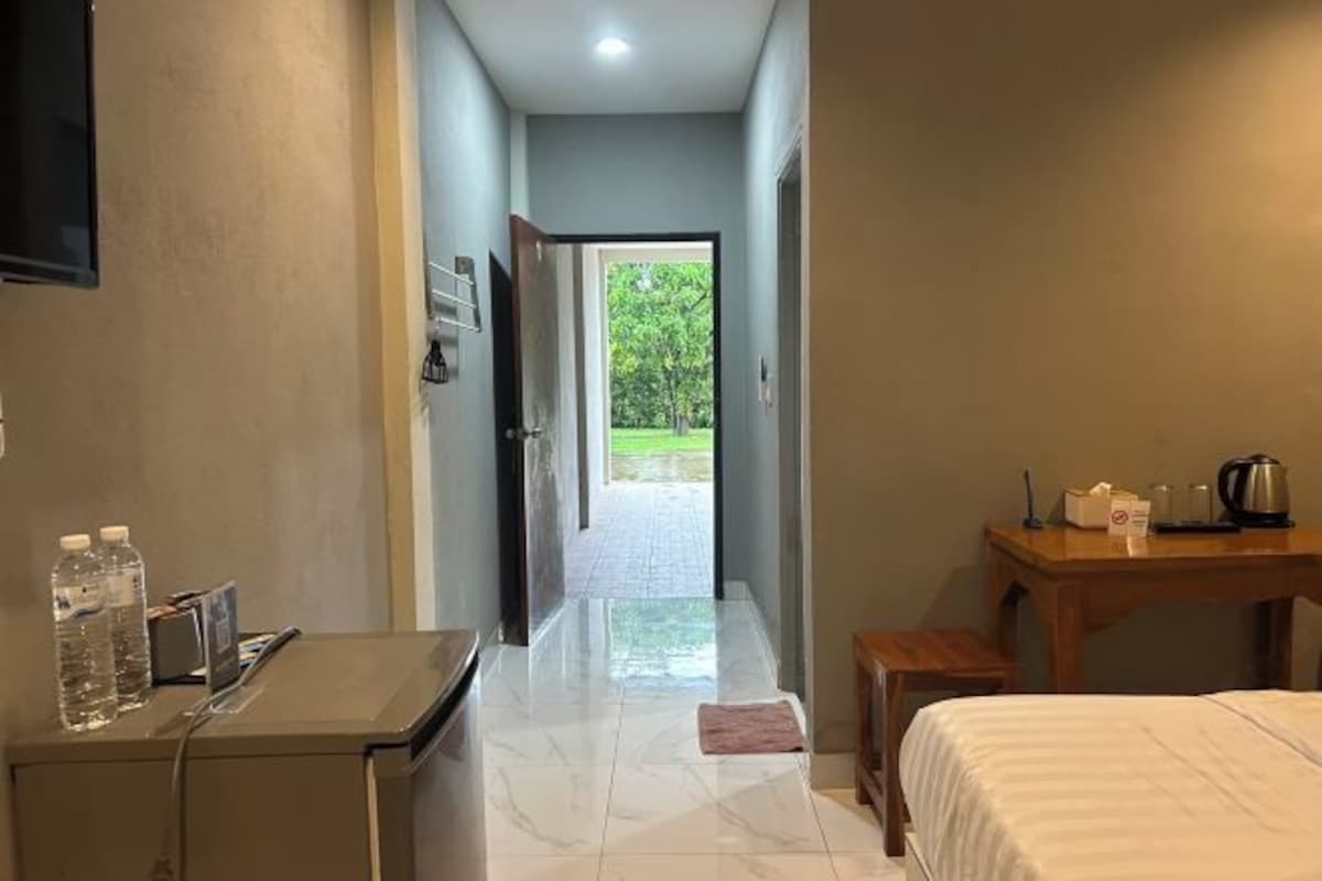 Habitación de hotel con cama, escritorio con hervidor, mesa con silla y vista a un jardín a través de una puerta abierta.