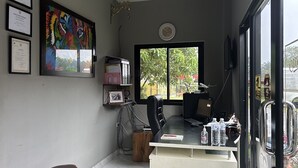 A small office with a desk, chair, and a large window. There are framed certificates on the wall and a colorful painting. - Baanmae Resort Thachana Suratthani (Tha Chana)