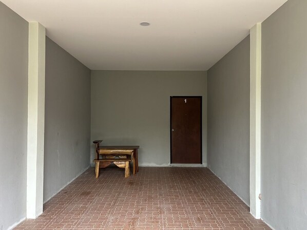 Un estrecho pasillo con un banco de madera, una puerta numerada con el número 1 y un piso de baldosas.