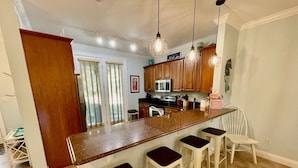 Una cocina con una isla central, taburetes de bar, armarios de madera, un microondas y una zona de comedor con sillas.