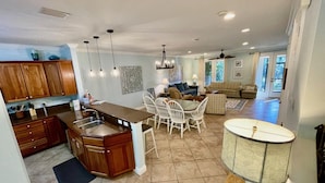 Una cocina amplia con una isla central, sillas de comedor blancas y una gran mesa de comedor. Hay una sala de estar con un sofá y una mesa de centro.