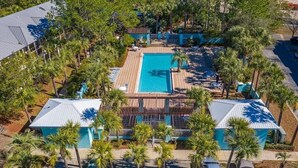 Vista aérea de un resort con una piscina central, rodeado de palmeras y dos edificios con techos azules.