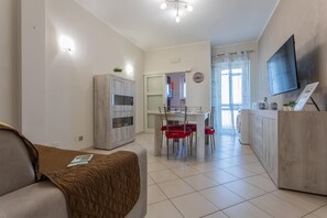 A modern living room with a sofa, a dining table with red chairs, a kitchen area, and a TV mounted on the wall. - La Casa di Marygrace by Wonderful Italy (Turin)