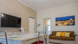 A modern living room with a dining area, a flat-screen TV mounted on the wall, and a painting of a cityscape. - La Casa di Marygrace by Wonderful Italy (Turin)