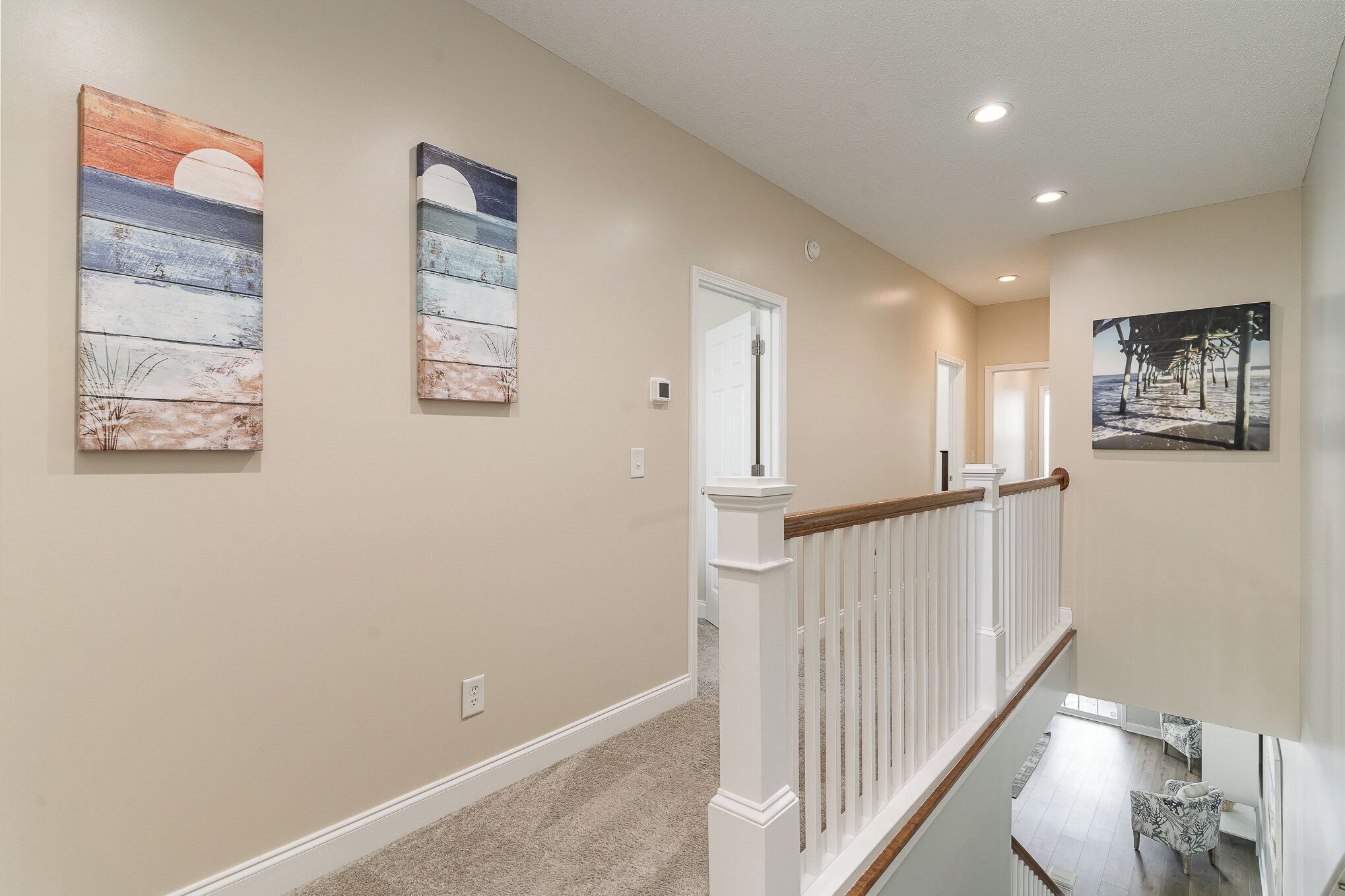 A hallway with beige walls, wooden railings, and artwork.