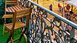 Un banc en bois avec une rambarde en métal, une zone herbeuse et un groupe de personnes à l’arrière-plan.