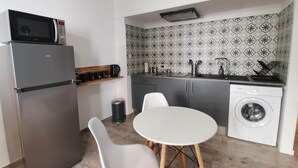 Une cuisine compacte équipée d’un réfrigérateur, d’un four à micro-ondes, d’un évier et d’un lave-linge. On y trouve également une petite table à manger avec deux chaises.