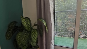 Une pièce avec une plante en pot, une porte-fenêtre coulissante et une vue sur un bâtiment et de la verdure à l’extérieur.