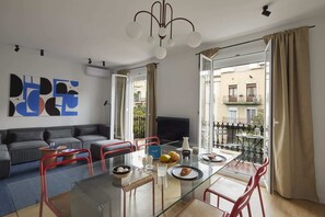 A modern living room with a glass dining table, red chairs, a grey sofa, and a TV. - Sweett | Rocafort 303 (Barcelona)