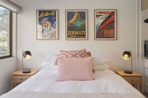 Een slaapkamer met een bed, twee nachtkastjes en drie ingelijste posters aan de muur.