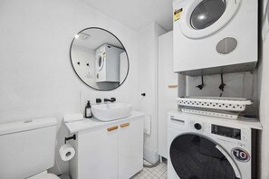 Un bagno compatto con WC, lavandino, specchio e lavatrice impilata.