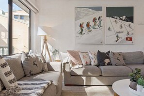 Een woonkamer met een bank, een lamp en twee wanddecoraties van skiërs.