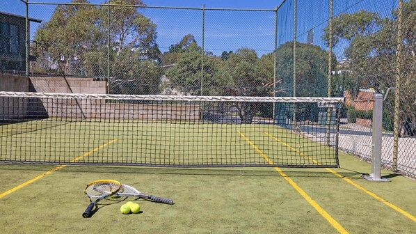 Una cancha de tenis con una red, dos raquetas y tres pelotas.