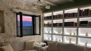 Ein gemütliches Wohnzimmer mit Steinwand, einem großen Fenster mit Aussicht, einer Bücherwand mit Büchern und Dekorationen sowie einem beigefarbenen Sofa.